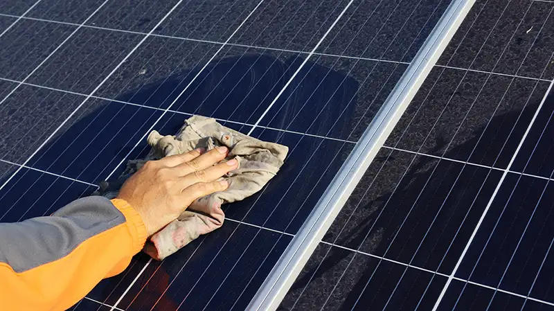 A person using a rag to clean dust from a solar panel.