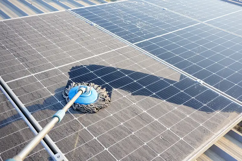 A broom being swept over dusty rooftop solar panels.