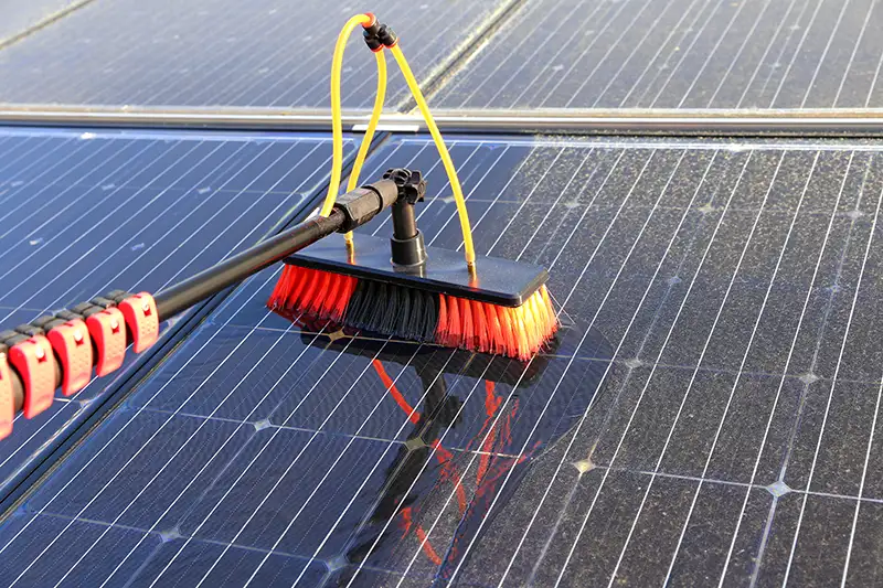 A broom with water hoses being used to gently clean a rooftop solar panel.