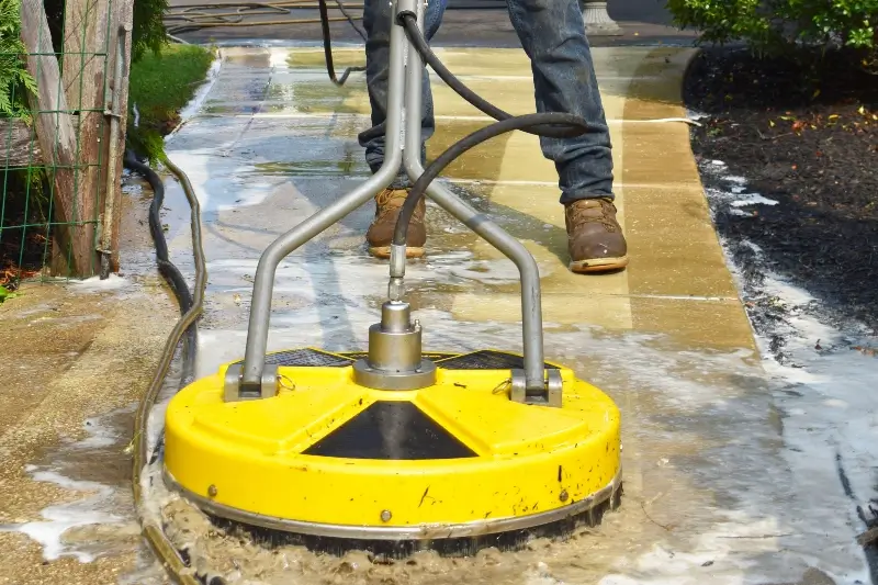 A worker pressure washing the sidewalk in front of a business