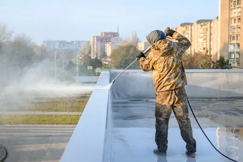 A worker using a pressure washer to clean a commercial roof