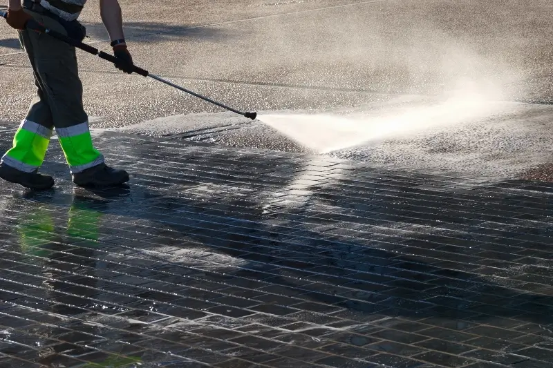 A worker holding a pressure washing hose and cleaning the sidewalk in front of a business